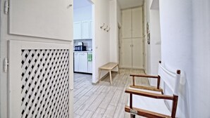 Käytävällä on puinen penkki, ovi, jossa on säleikkömäinen tuuletusaukko, ja näkymä keittiötilaan, jossa on kaappeja ja mikroaaltouuni.