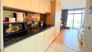 A modern kitchen with a black countertop, white cabinets, and a coffee maker. There is a dining area with a table and chairs, and a large window offering a view of the city. - The Straits Residence by Koala (Malacca City)