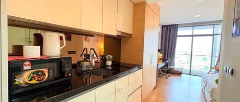 Una cocina moderna con encimera negra, armarios blancos y una cafetera. Hay un comedor con mesa y sillas, y un ventanal con vistas a la ciudad.