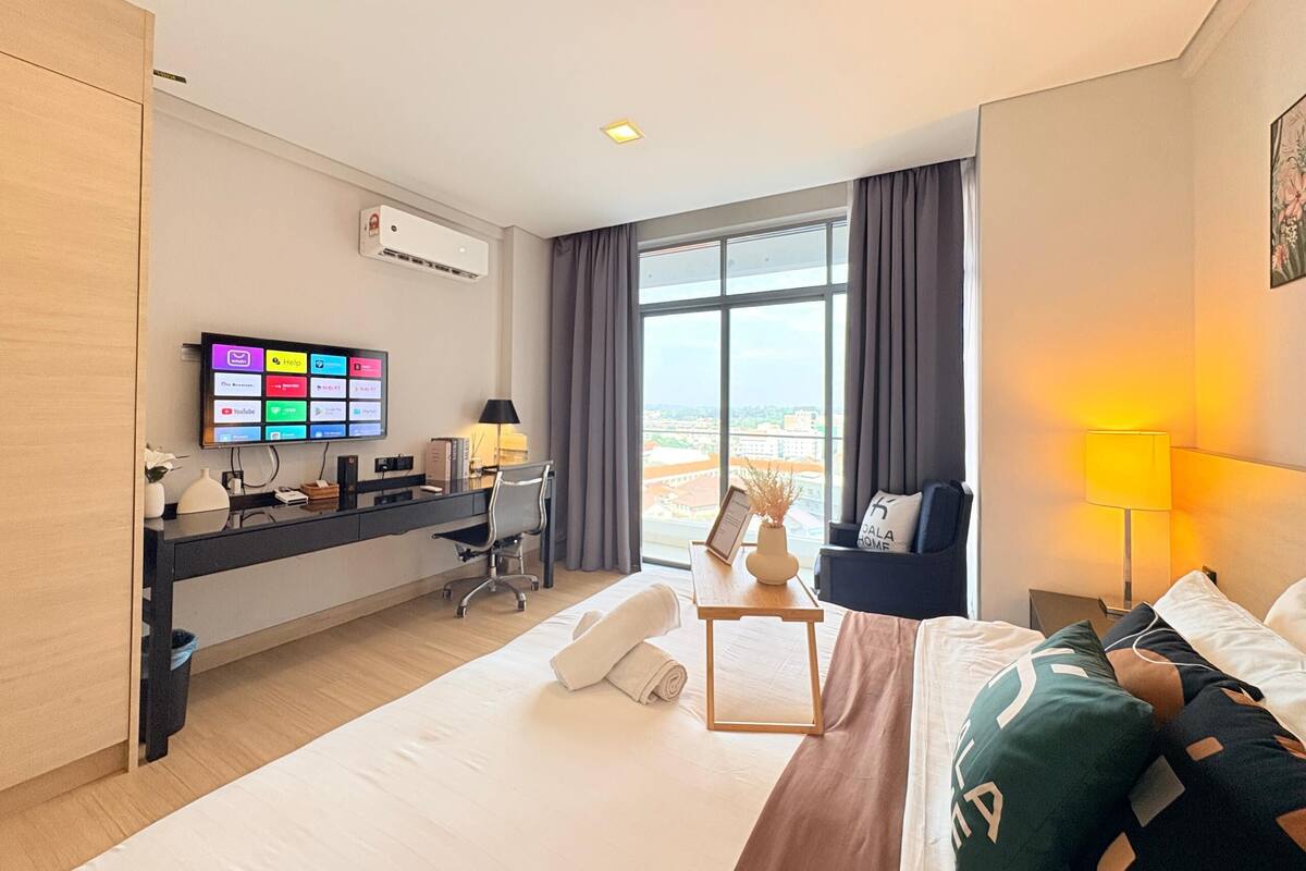 Een hotelkamer met een bed, een bureau met een computer, een televisie en een raam met uitzicht.