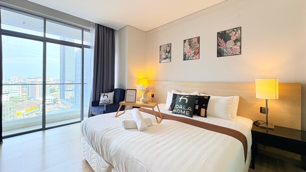 A modern hotel room with a large bed, a desk, a chair, and a view of the city through floor-to-ceiling windows. - The Straits Residence by Koala (Malacca City)
