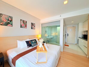 Une chambre d’hôtel comprenant un lit, une table de chevet, une douche en verre et un coin cuisine.