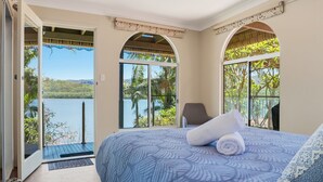 A bedroom with a large bed, a chair, and a view of a lake through arched windows. - Dorathee Cottage - Pet Friendly - Absolute Waterfront (Gunderman)