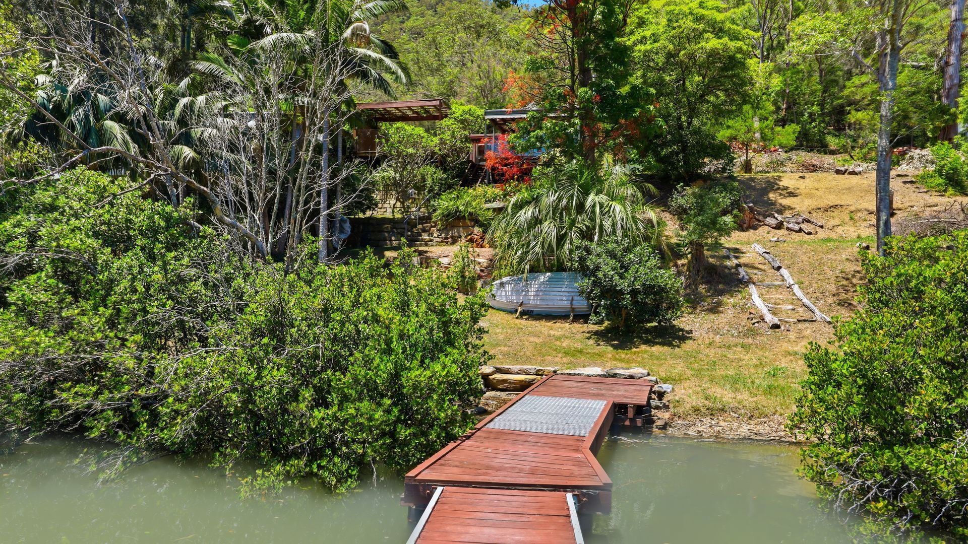 A wooden dock extending into a body of water, surrounded by dense greenery and a small structure in the background.