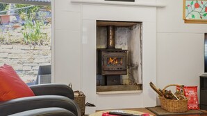 A cozy living room with a stone wall, a fireplace, a wicker basket with firewood, and a red fire blanket on the floor. - Dorathee Cottage - Pet Friendly - Absolute Waterfront (Gunderman)