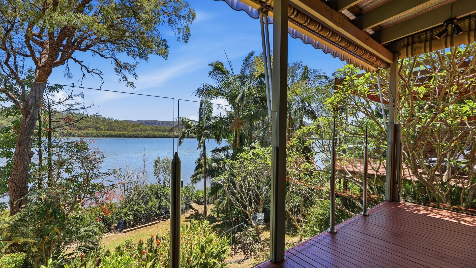 Terraza de madera con vista a un lago, rodeada de vegetación densa y un cielo despejado.
