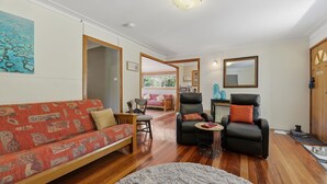 A living room with a red patterned sofa, two black leather chairs, a small round table, and a grey rug. - Dorathee Cottage - Pet Friendly - Absolute Waterfront (Gunderman)