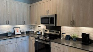 Une cuisine moderne avec des meubles en bois clair, des appareils en acier inoxydable et un plan de travail noir.