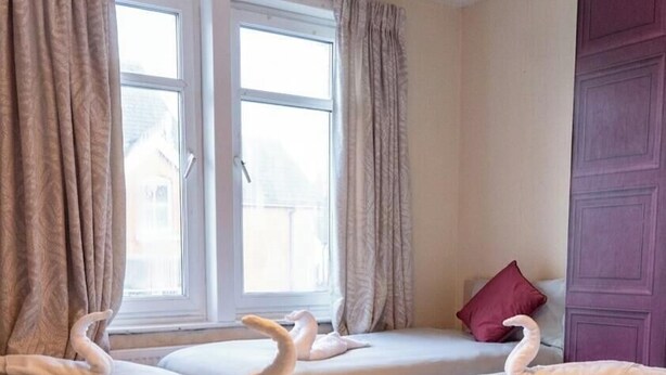 A hotel room with two beds, a window with curtains, and a purple door. - Estokova Haven sleeps up to 9 - Free parking (Swindon)