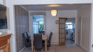 A modern living room with a sofa, a dining table with chairs, a fireplace, and a kitchen in the background. - Estokova Haven sleeps up to 9 - Free parking (Swindon)