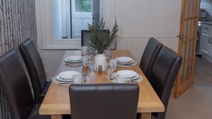A dining area with a wooden table set for four, surrounded by leather chairs. A potted plant and a clock are on the wall. - Estokova Haven sleeps up to 9 - Free parking (Swindon)