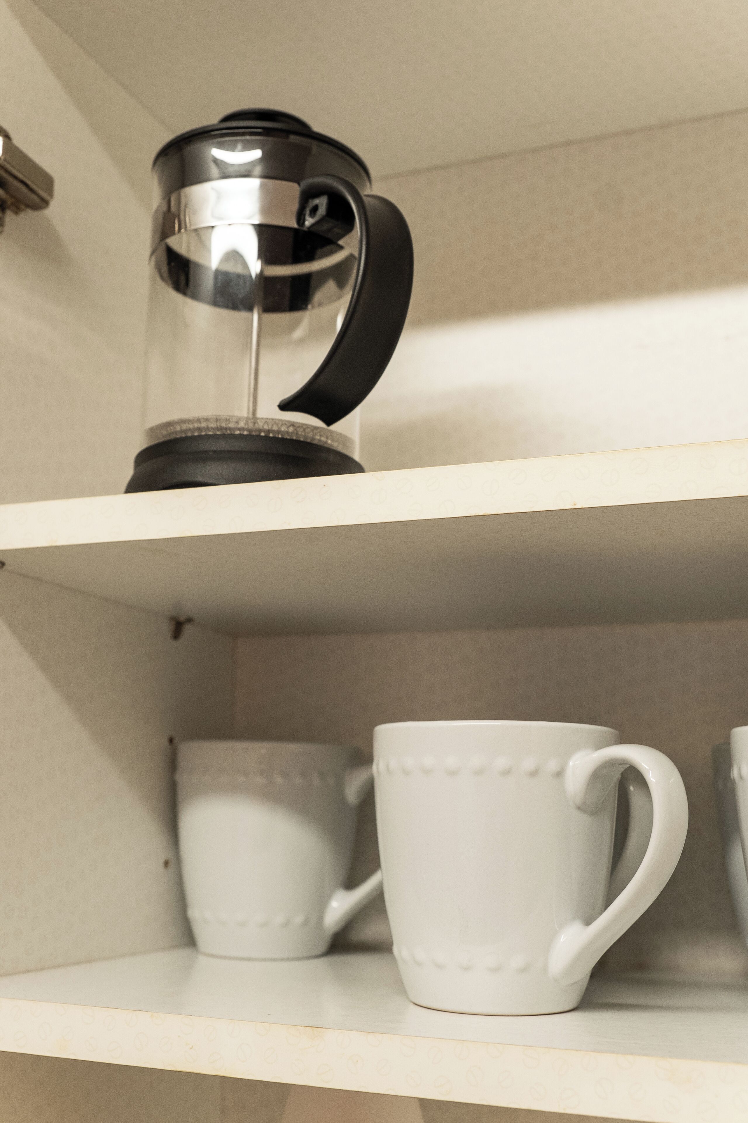A shelf with a coffee maker and white mugs.