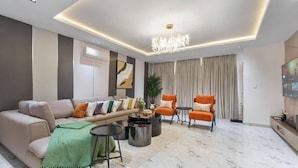 A modern living room with a sofa, armchairs, a coffee table, and a TV. - Regent Service Apartment  (Abuja)