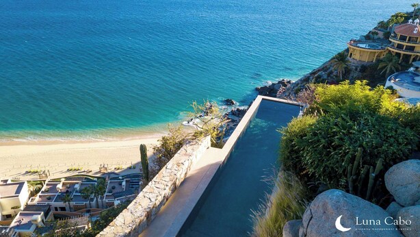 Uma propriedade costeira com piscina infinita privativa com vista para a praia, uma parede de pedra de contenção e vista do oceano.