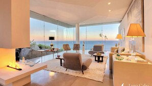 Uma sala de estar moderna com vista para o mar, uma lareira e uma área de estar com tapete.