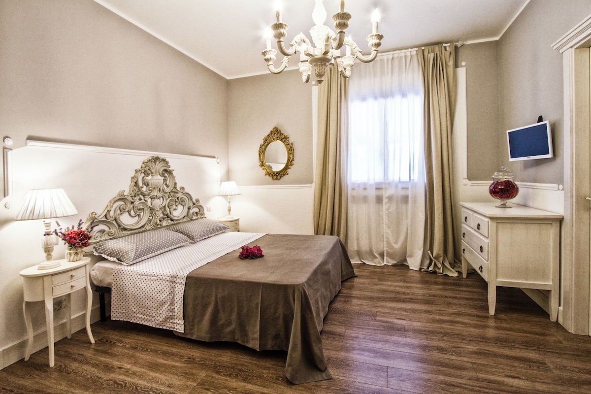 A bedroom with a large bed, a nightstand, a dresser, a mirror, and a chandelier.