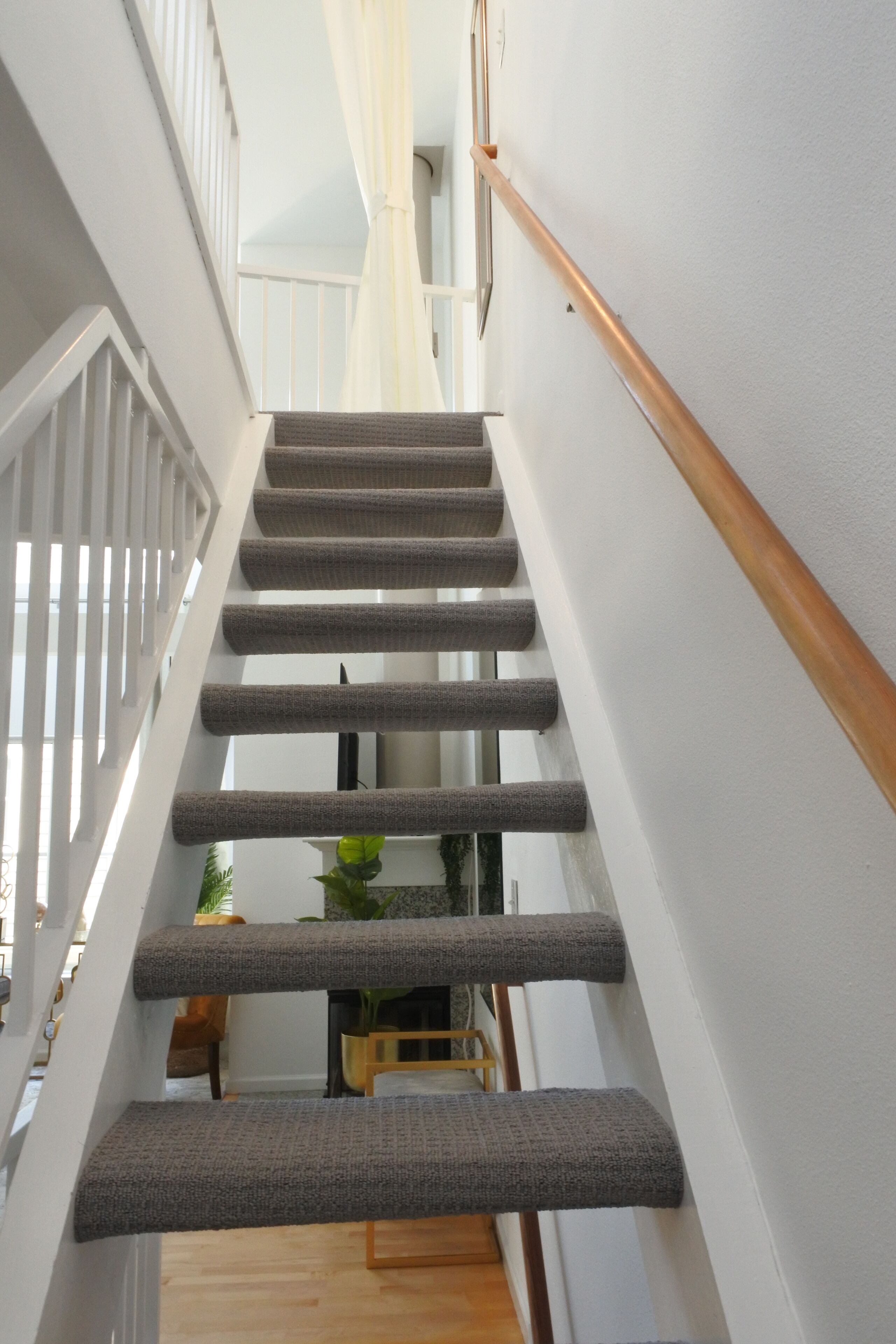 A staircase with a wooden handrail and grey carpeted steps leading to an upper floor.