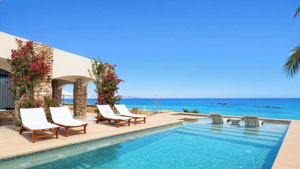 A clear blue pool with white lounge chairs, stone pillars, and a view of the ocean. - Oceanfront Villa · Heated Pool, Fire Pit & Beach (San José del Cabo)