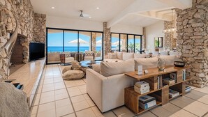 A spacious living area with a stone wall, a large sofa, a coffee table, and a bookshelf. - Oceanfront Villa · Heated Pool, Fire Pit & Beach (San José del Cabo)