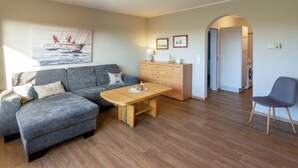 Ein modernes Wohnzimmer mit grauem Sofa, Couchtisch aus Holz und einer kleinen Kommode.