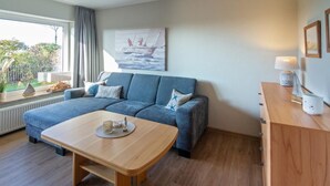 Ein modernes Wohnzimmer mit einer Couch, einem Holztisch und Blick ins Freie durch ein großes Fenster.