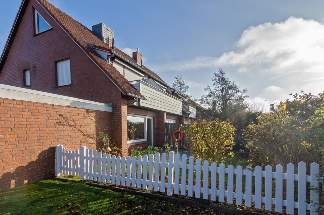 A two-story brick house with a white picket fence, a visible window, and a clear sky.