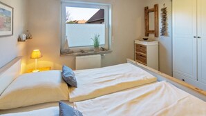 Ein Schlafzimmer mit zwei Betten, einem Fenster, einer Heizung, einer Lampe, einer Pflanze und einem Kleiderschrank.
