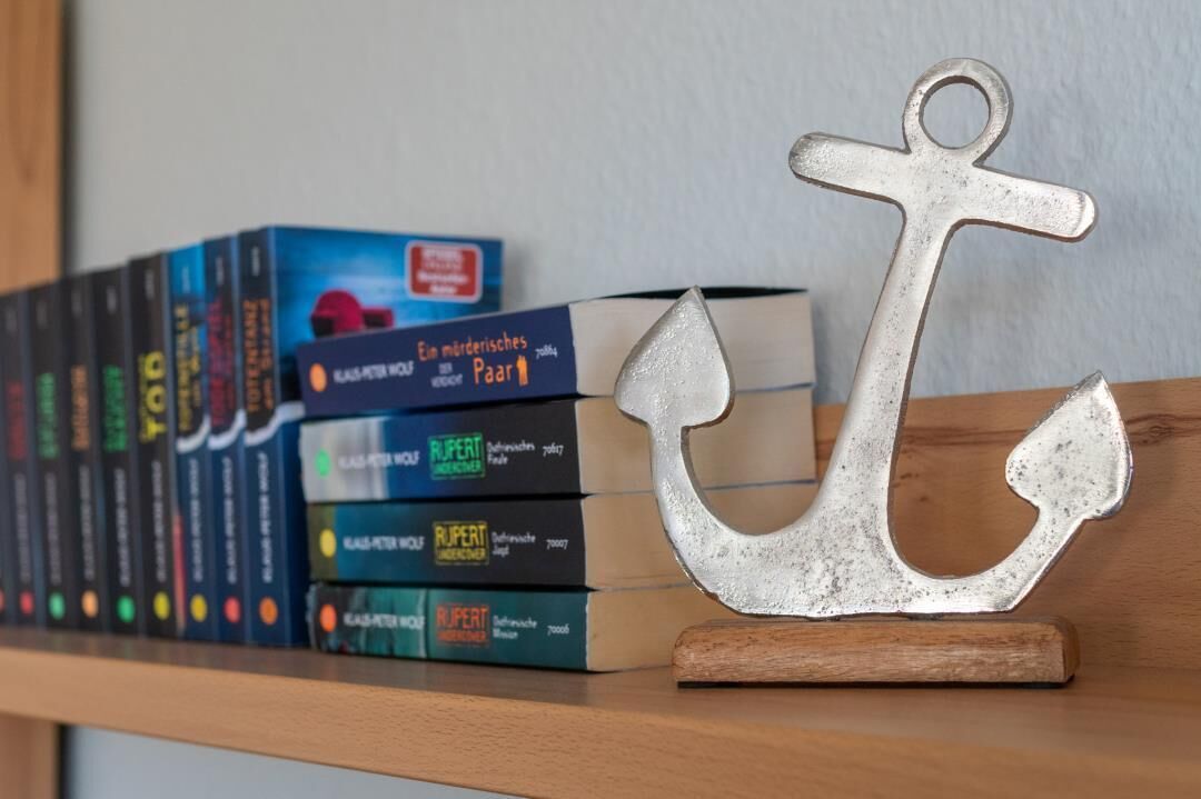 A bookshelf with a metal anchor decoration and several books.
