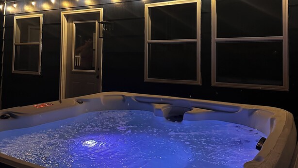 Un bain à remous doté d’un éclairage bleu, entouré de quatre fenêtres au-dessus desquelles sont fixés des luminaires.