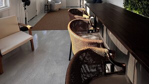 Un intérieur moderne avec un long comptoir en bois, des chaises en osier, un ventilateur de plafond et une vue sur l’extérieur grâce à de grandes fenêtres.