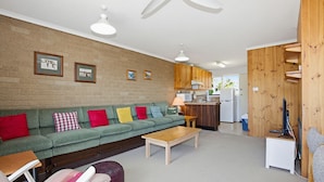 Ein gemütliches Wohnzimmer mit einem grünen Sofa, Holzschränken und einer Küchenzeile inklusive Kühlschrank und Mikrowelle.