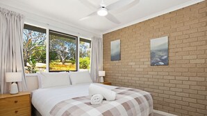Ein Schlafzimmer mit einem großen Bett, zwei Nachttischen, einem Deckenventilator und einer Ziegelwand mit zwei gerahmten Bildern.