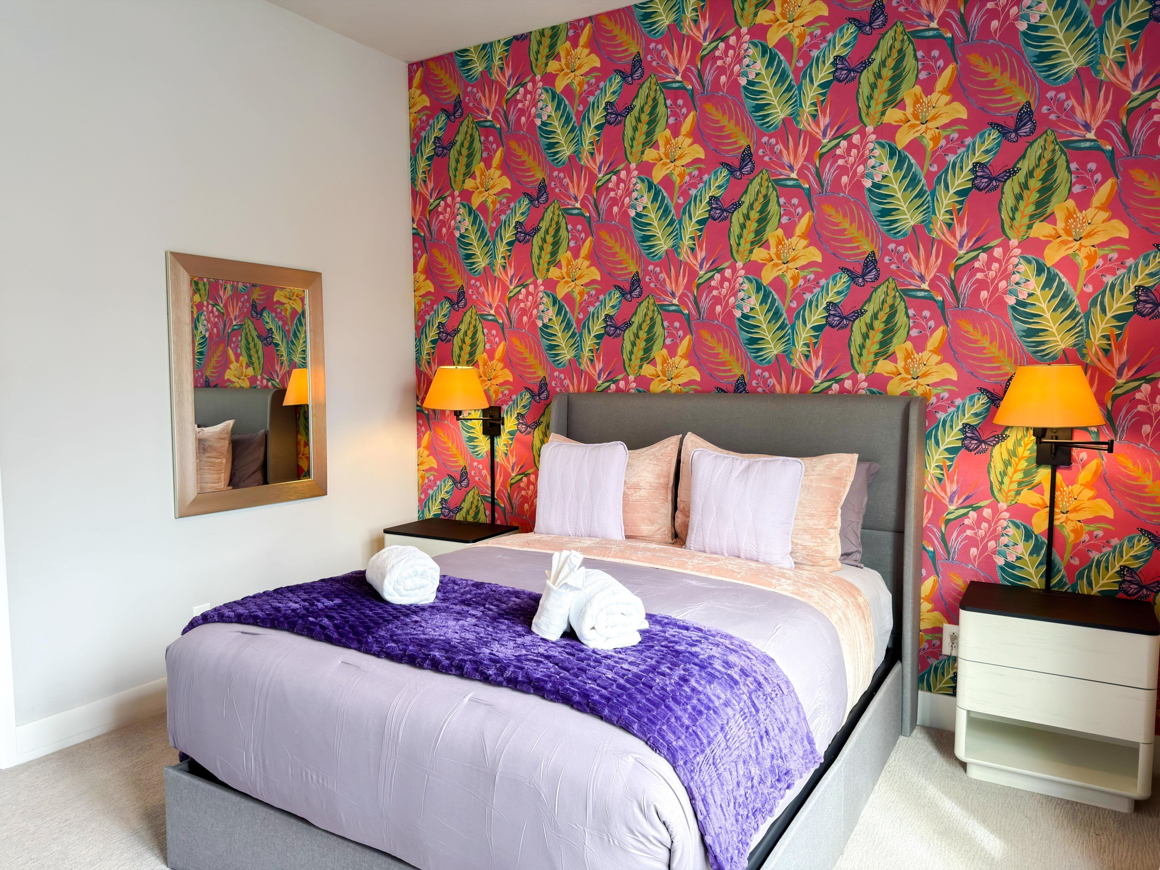 Ein Hotelzimmer mit einem großen Bett, zwei Nachttischlampen, einem Nachttisch und einem Spiegel an der Wand.