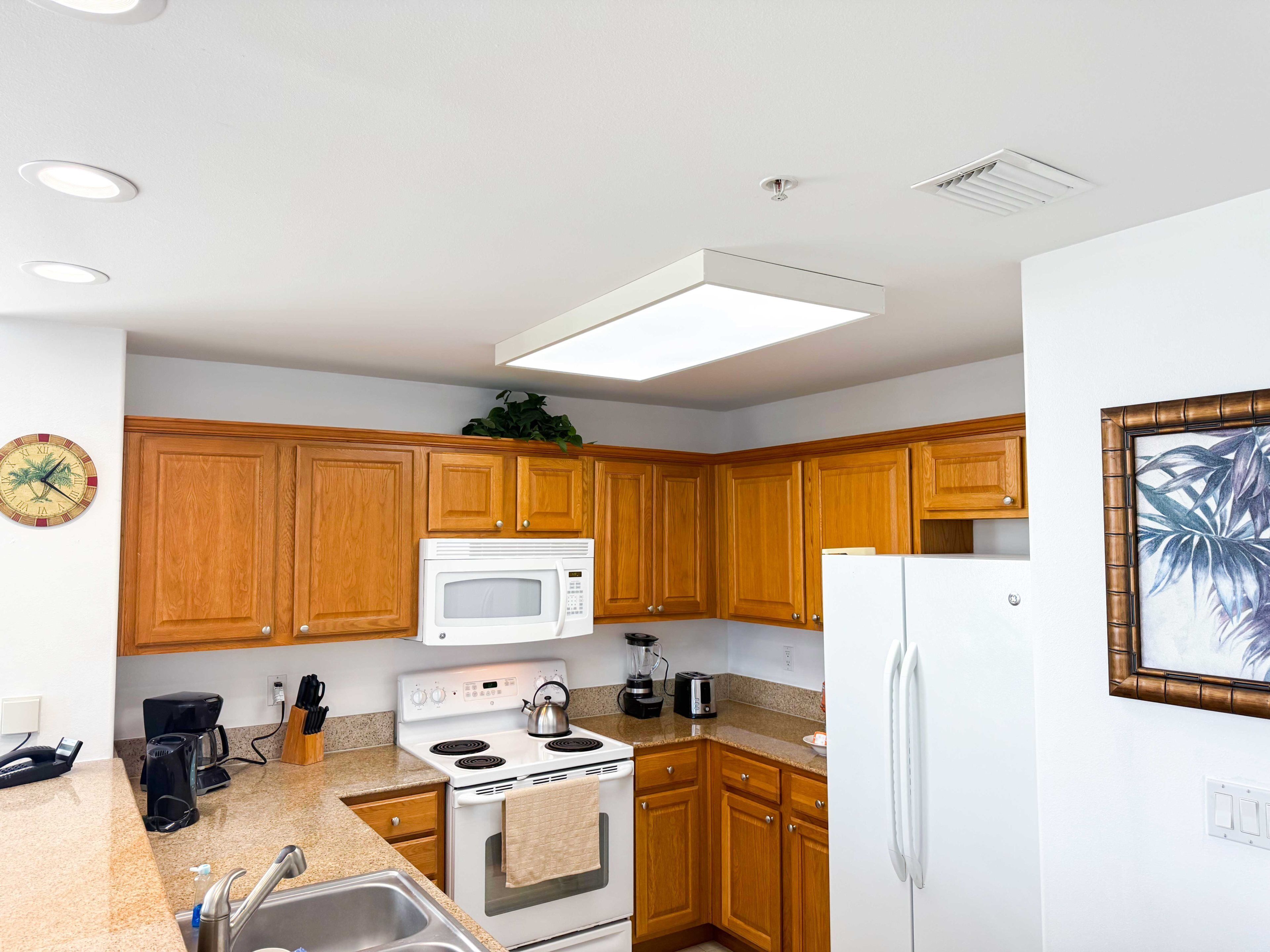 A kitchen with wooden cabinets, a white microwave, a stove, a sink, and a refrigerator.