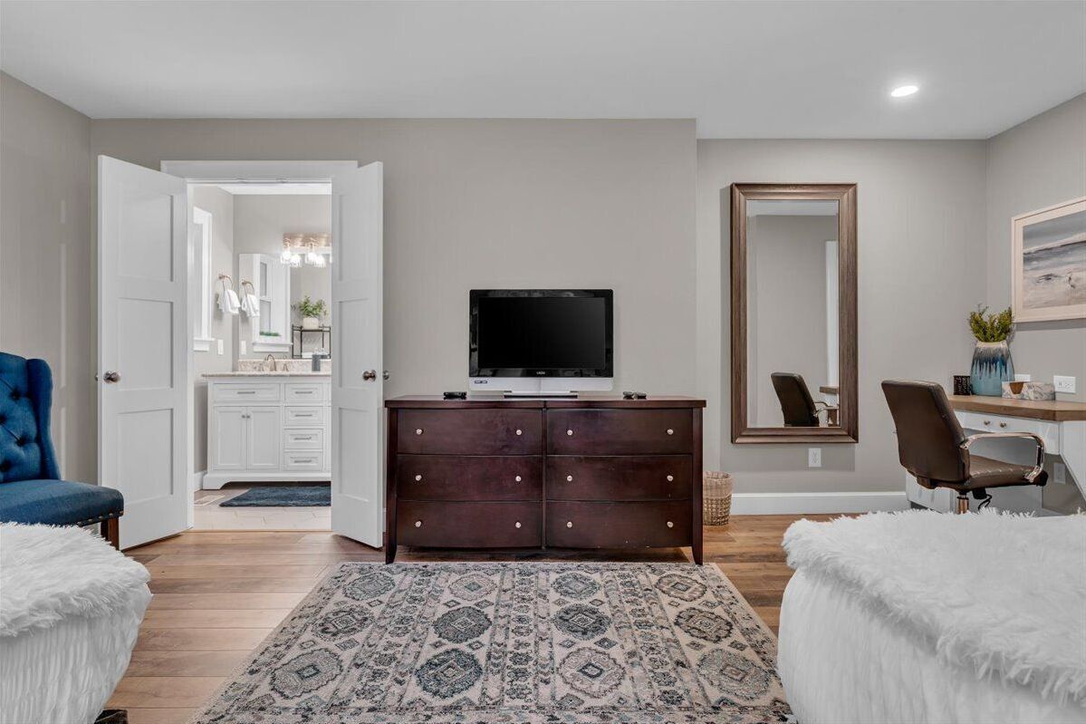 A modern bedroom with a television, a large mirror, a dresser, and a patterned rug.