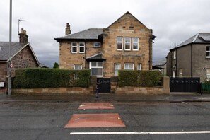 A stone building with a pitched roof, a gated entrance, and a speed limit sign. - Stirling Edwardian House: Fireplace/Garden/Parking (Stirling)