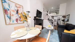 Moderni olohuone, jossa on ruokailutila, musta nahkasohva, portaikko ja seinälle asennettu televisio.