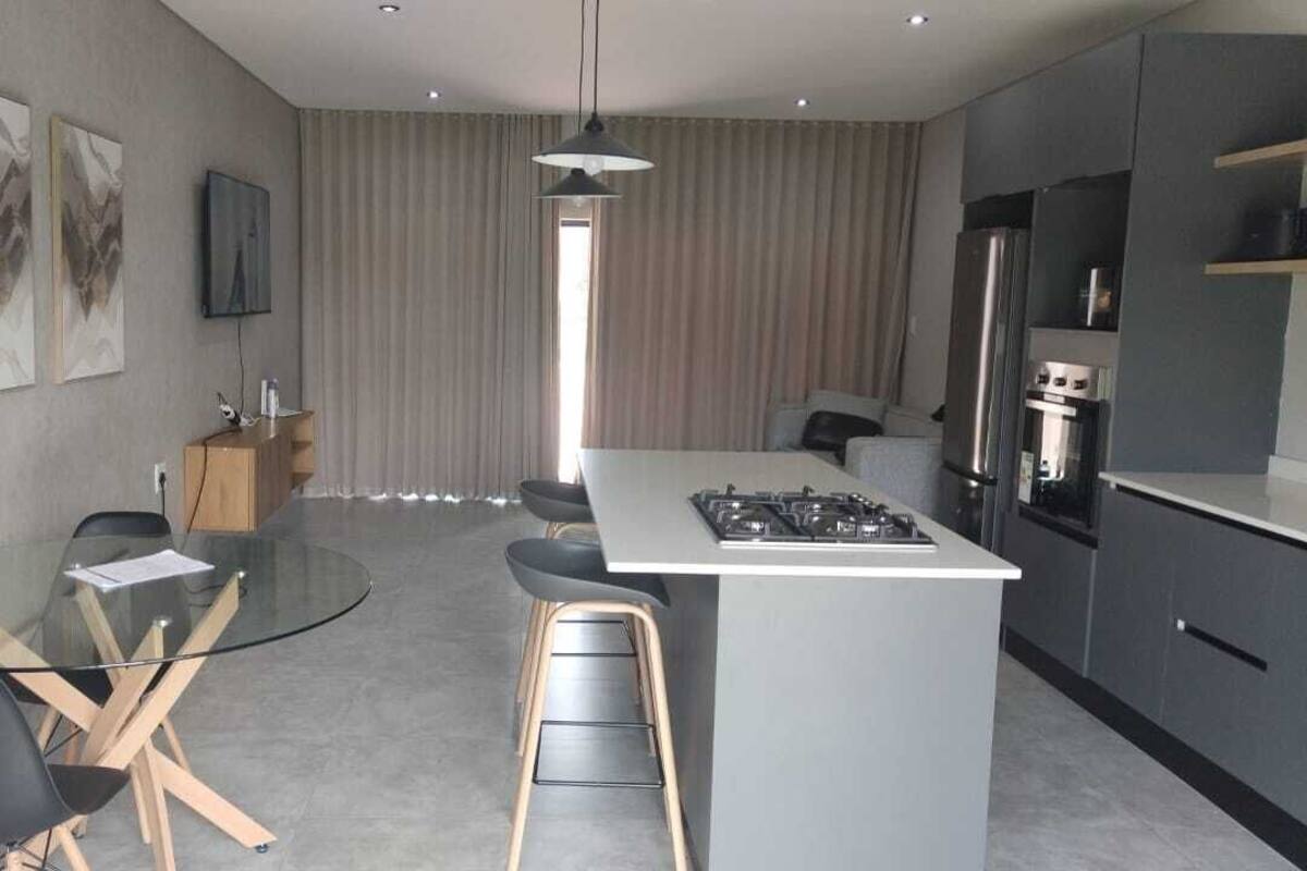 A modern kitchen with a central island, bar stools, a dining table with chairs, and a TV mounted on the wall.