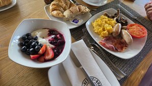 Ein Frühstückstisch mit Croissants, Rührei, Würstchen, Tomaten und einem Joghurt mit Beeren.