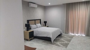 Ein modernes Schlafzimmer mit Bett, Nachttischen, einem Wandklimagerät und einem Fenster mit Vorhängen.