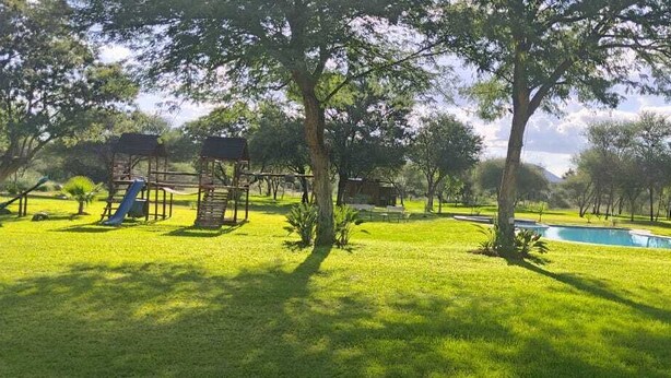 Eine Parkanlage mit Rasen, einem Spielplatz, einem kleinen Pool und Bäumen.