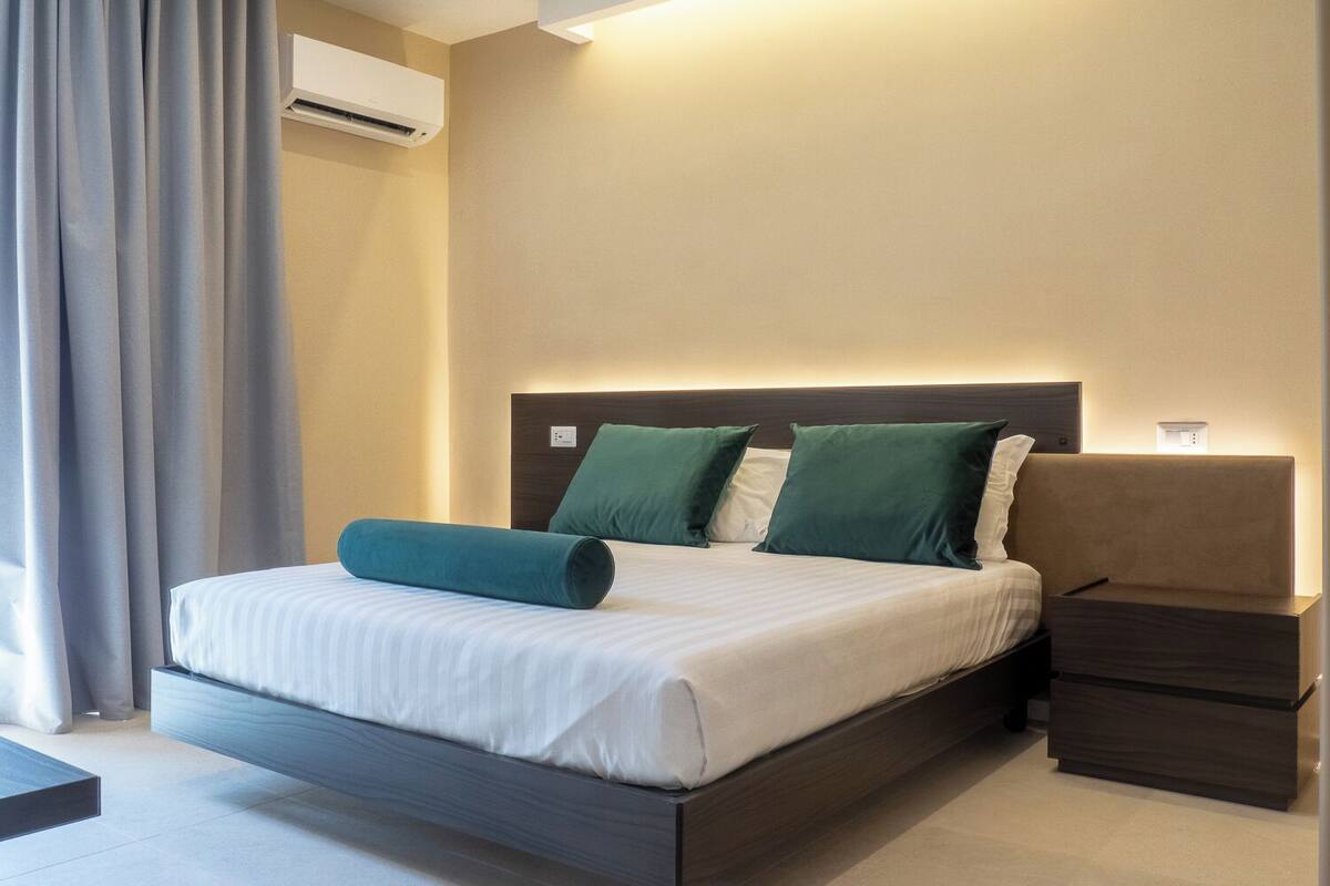 A modern hotel room with a bed, a nightstand, and an air conditioning unit.