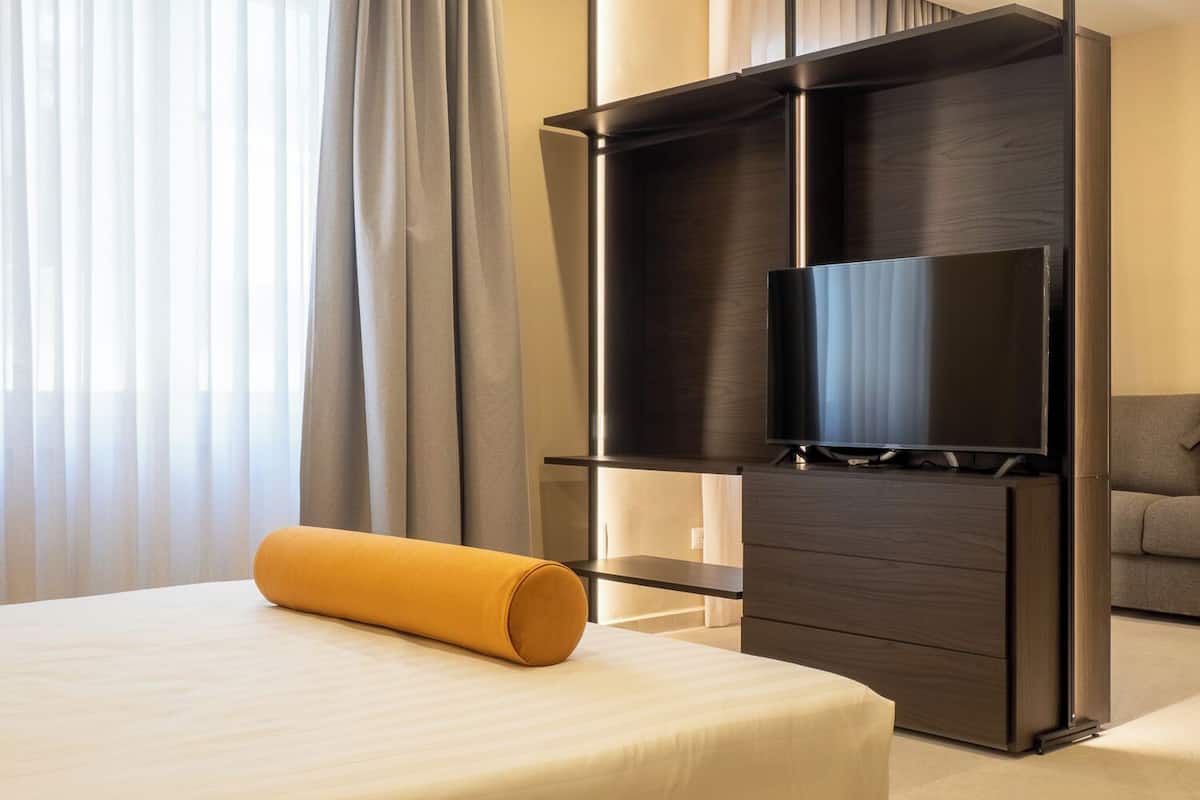 A hotel room with a bed, a TV on a wooden stand, and a sofa.