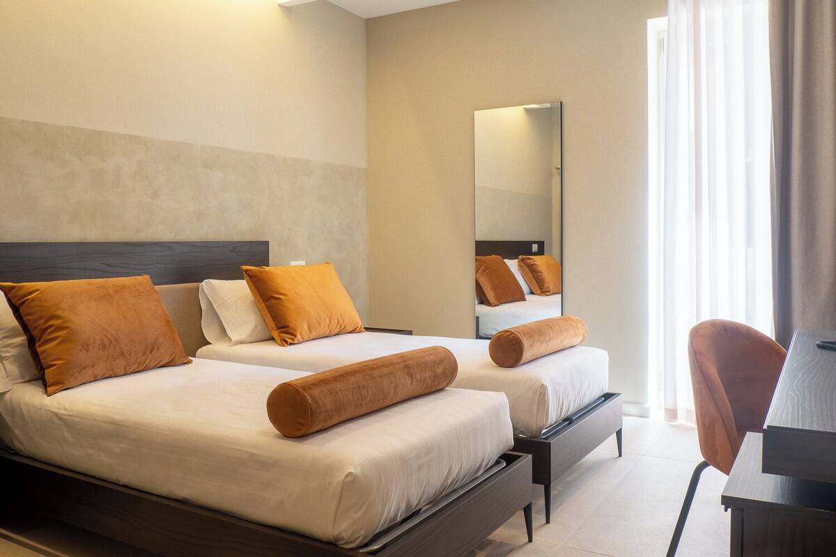 A hotel room with two beds, a large mirror, and a desk with a chair.