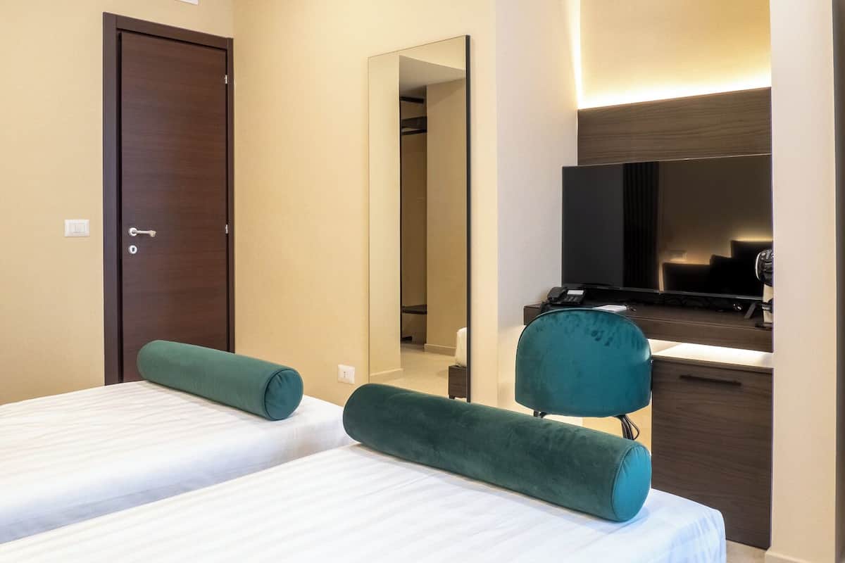 A hotel room with two single beds, a desk with a chair, a television, and a mirror.