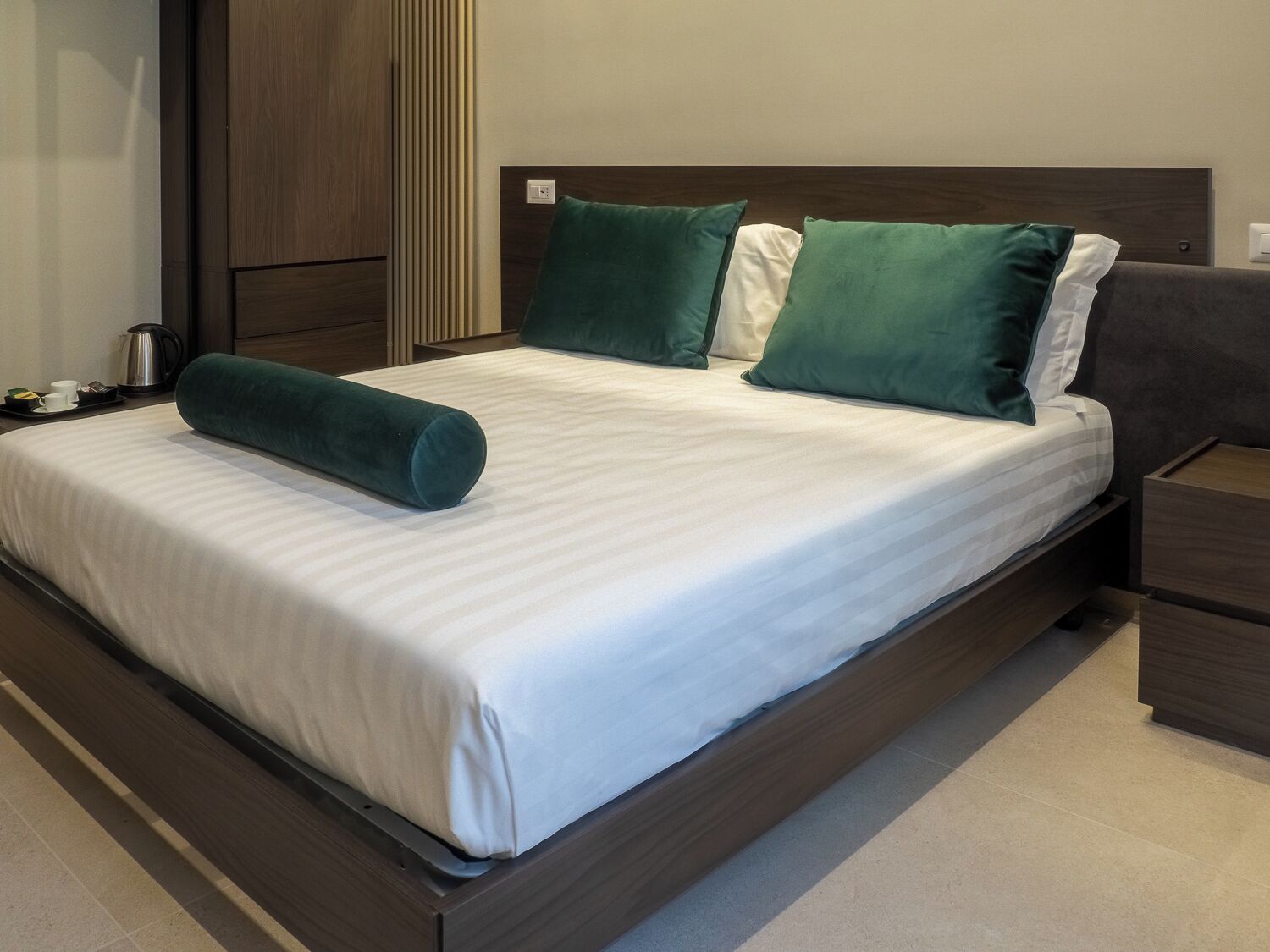 A neatly made bed with a white and green striped bedspread, two green pillows, and a green cylindrical pillow.