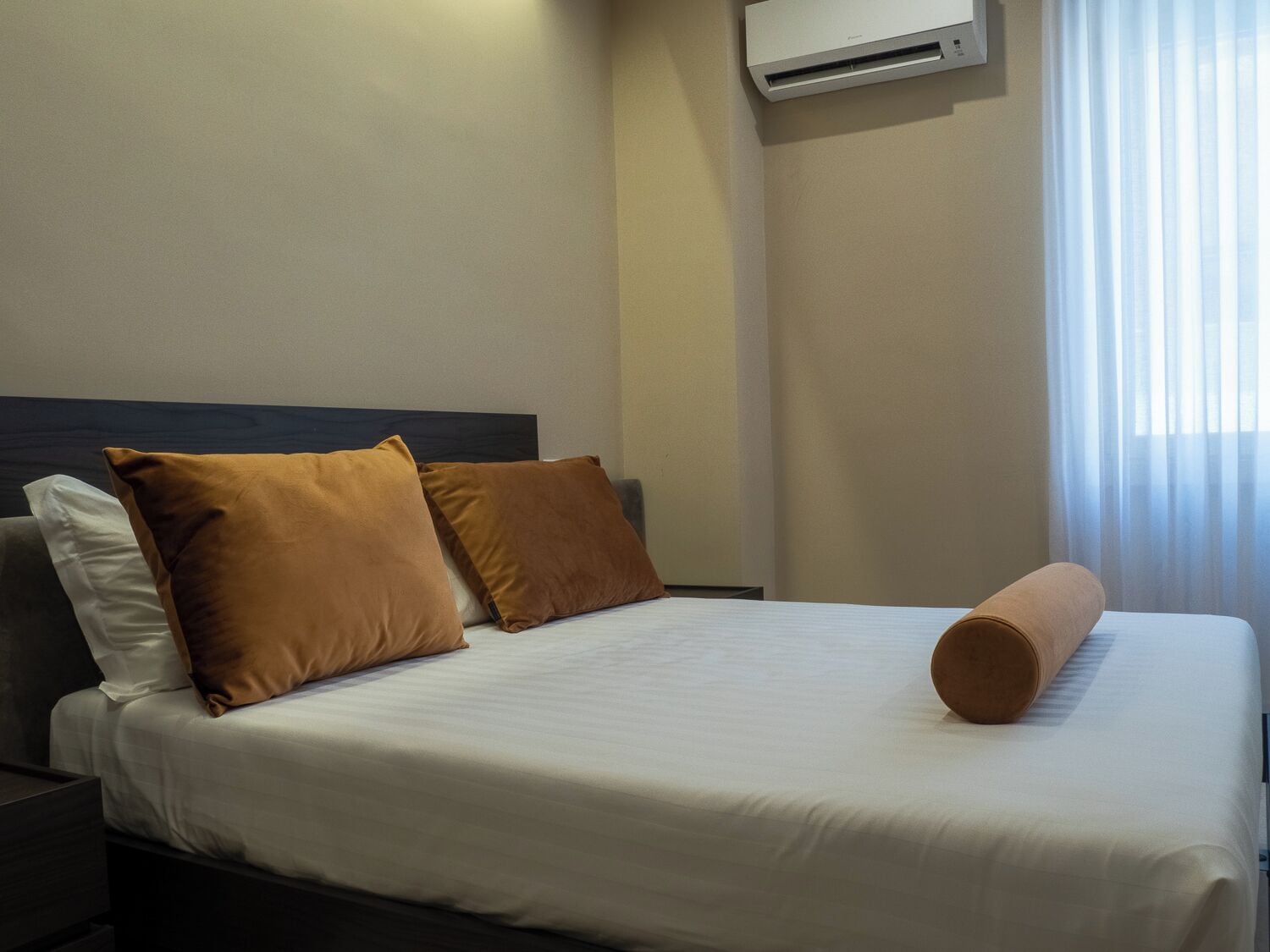 A neatly made bed with white and brown bedding, a dark headboard, and a rolled-up beige towel.