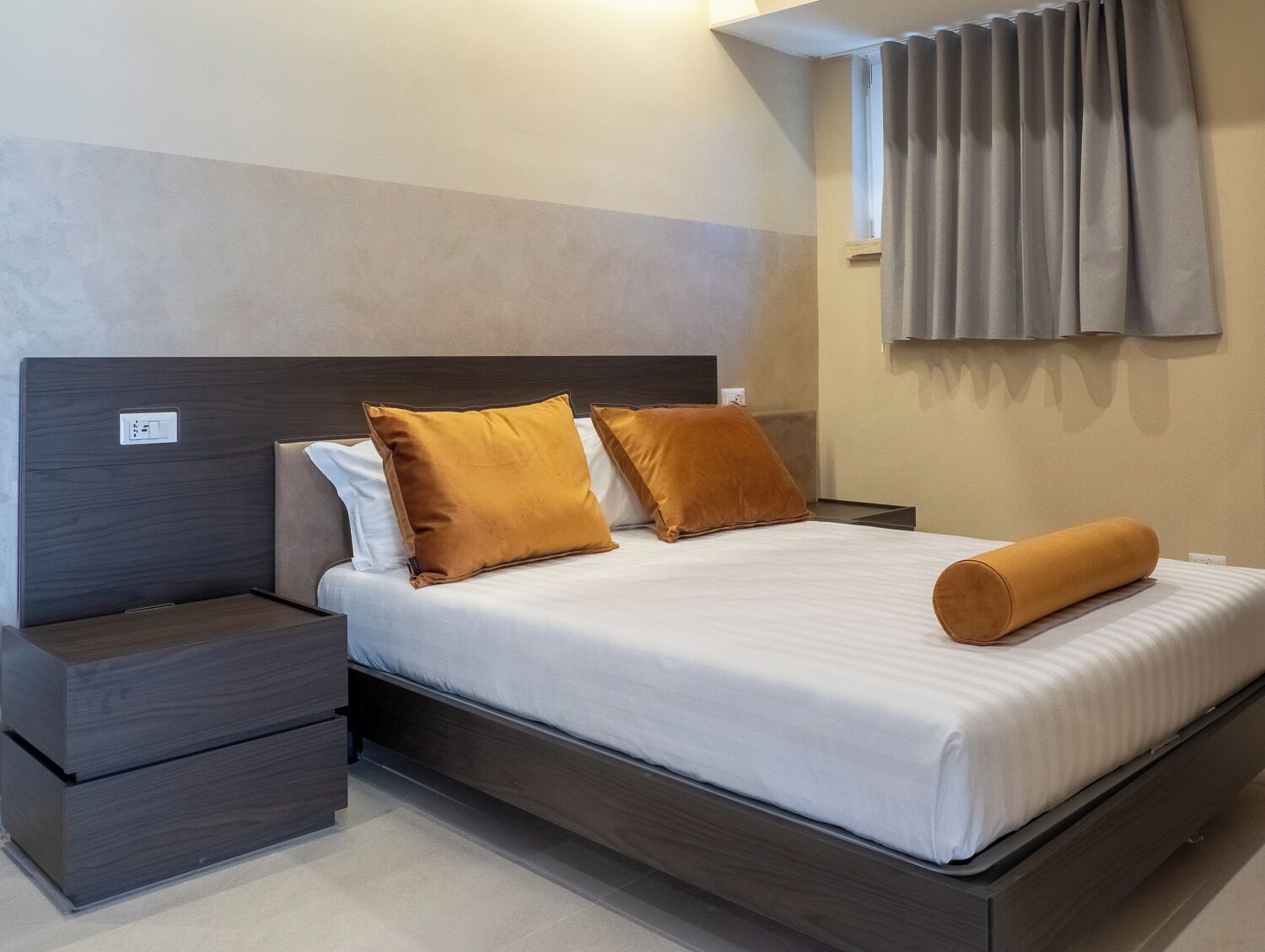 Een moderne hotelkamer met een groot bed, twee nachtkastjes, een hoofdbord en een raam met gordijnen.