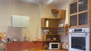 Eine kompakte Küche mit Mikrowelle, Backofen und einem Bosch-Kühlschrank. Es gibt einen Holzkasten mit Glastüren und einen kleinen Esstisch mit Stühlen.