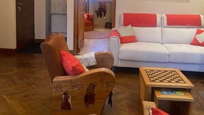 Ein Wohnzimmer mit Holzboden, einem braunen Sessel, einem weißen Sofa mit roten Kissen und einem Holztisch.